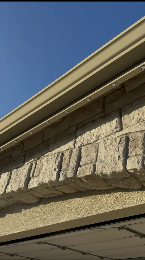 Permanent lighting track running along the eave above a stone facade in daylight